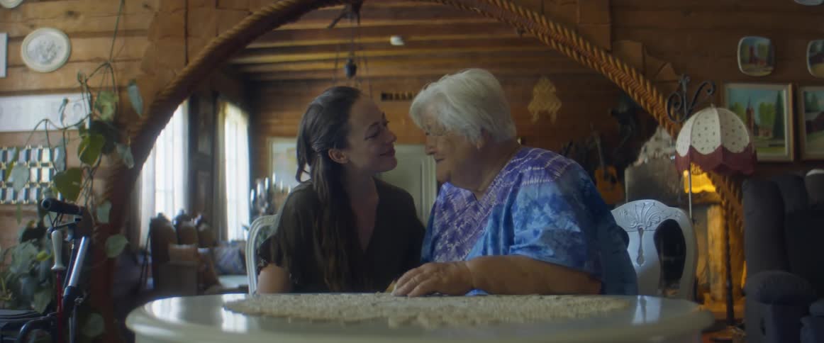 Granddaughter hugs her grandmother while sitting at a table with a lace tablecloth on it