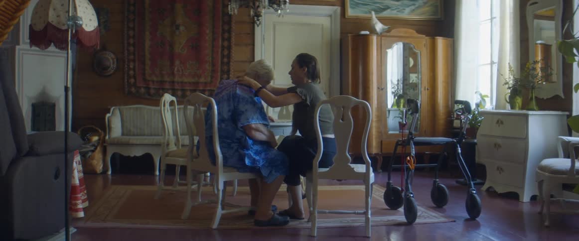 Granddaughter massages the shoulders of her grandmother as they sit in white chairs