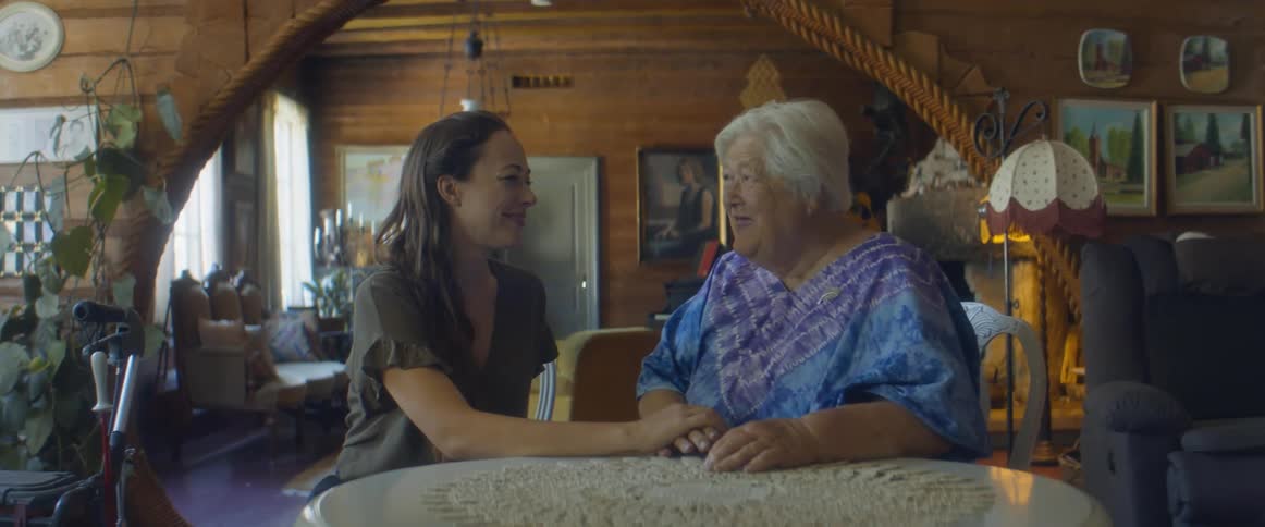 A woman places her hand on her mothers hand as they sit and talk at home