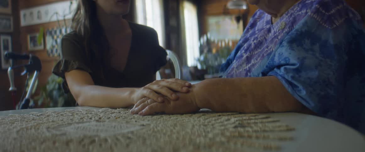 A young and elderly woman sit together holding hands at a dining table