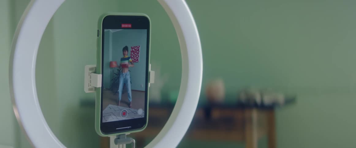 A smartphone in a stand records a woman dancing until she stops recording
