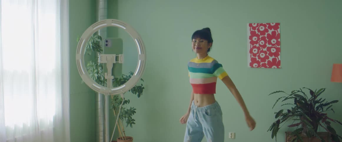 Woman with colourful t shirt glasses and jeans dances and records herself on iphone smartphone