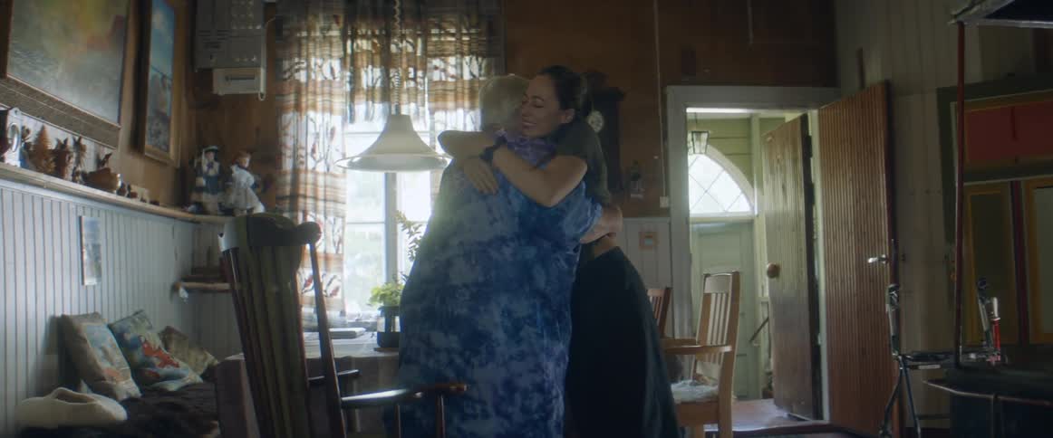 A young woman walks into a home and an elderly woman inside stands up to hug her