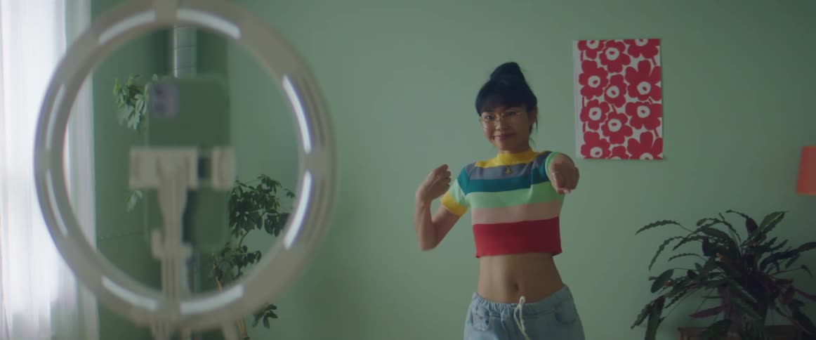 A young woman dances while recording herself with a smartphone attached to a smartphone stand
