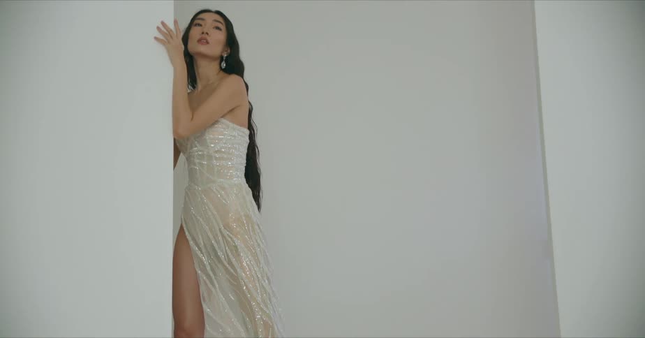 A model in a white and gold gown stand holding a wall looking up