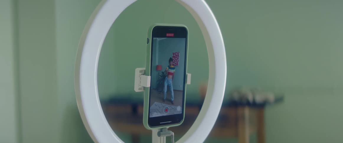 A girl records herself dancing in her bedroom with her smartphone in a ring light