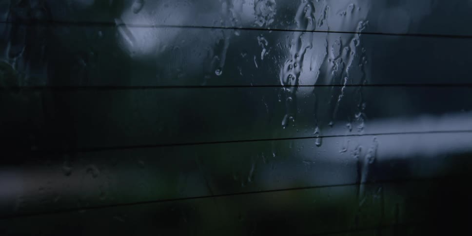Rain slides down glass of window decorated with horizontal lines as window wiper blades move