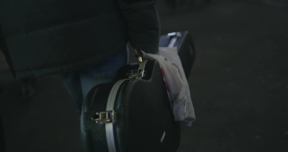 Close up of a person walking with a guitar case in hand