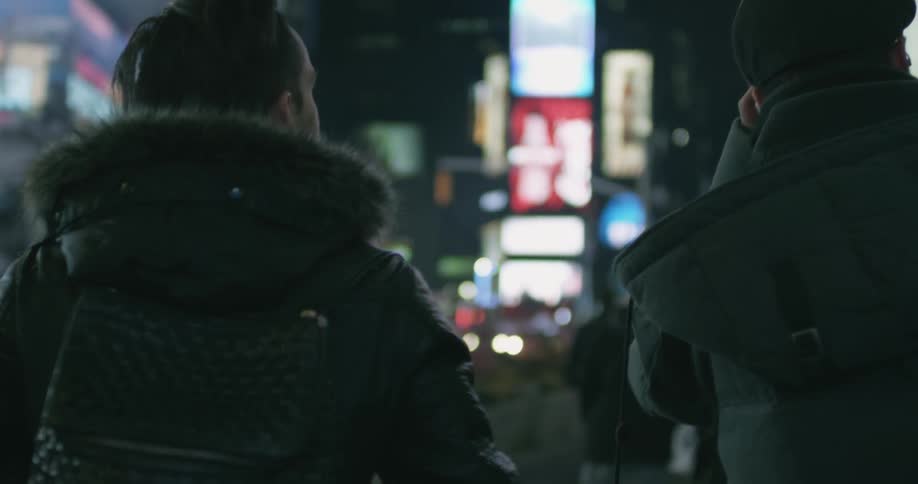 A group of people wearing coats walk down a well lit city street