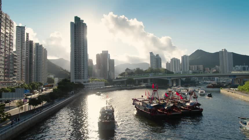 Boats travel in the river next to a city as traffic travels on the city street