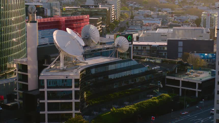 Satellite dishes sit on the rooftop in the city while cars travel on the streets below