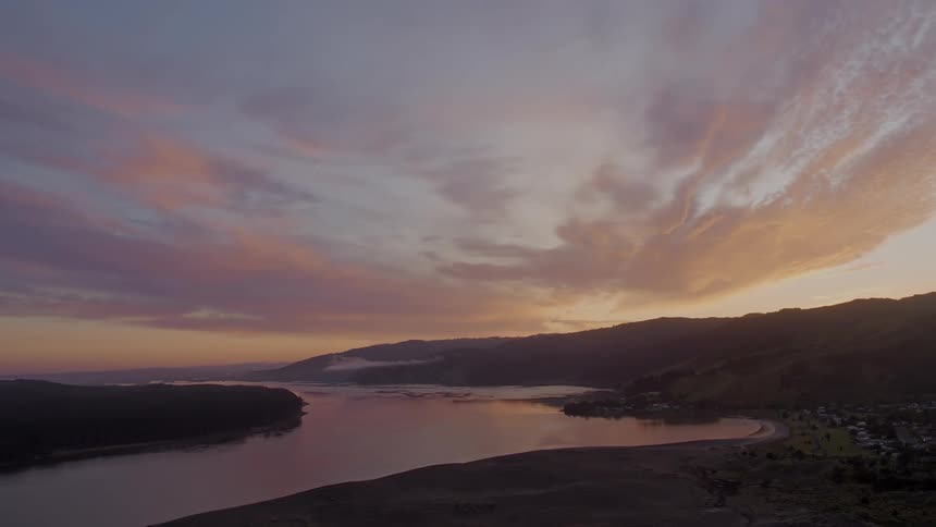 The sun sets over a winding river along the coast