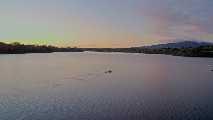 Two people paddling a kayak across a lake with trees and mountains in the distance