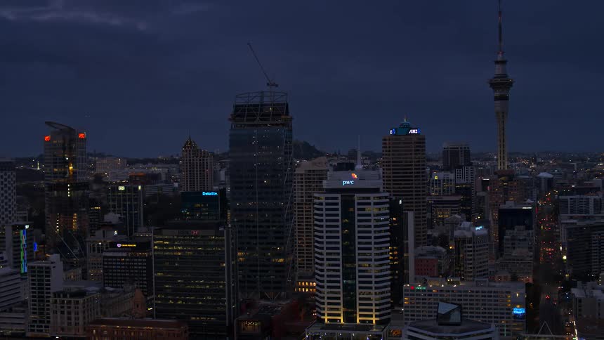 A construction crane sits atop a skyscraper in a city skyline at night