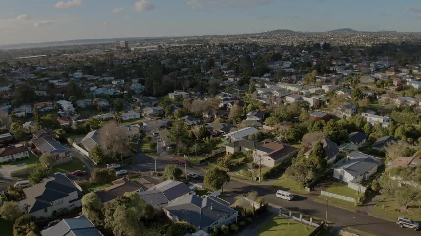 Shadow covers center of suburb stretching to water and hills on misty horizon as van drives along street
