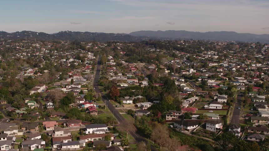 Traffic drives down street past through large neighborhood of houses toward mist covered forested mountains