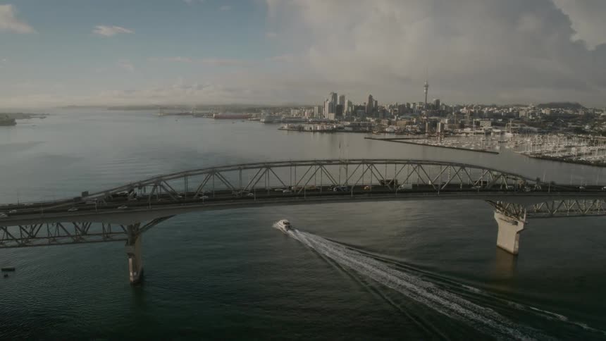 A boat travels under a traffic bridge off the coast of a metropolis during the day