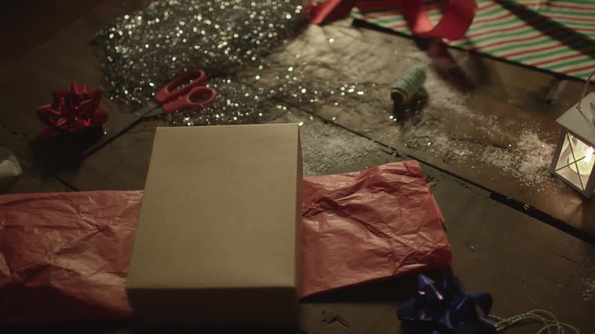 An unwrapped box, some tinsel, scissors and wrapping paper on a wood floor