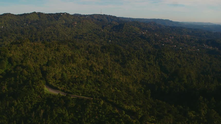 A landscape with hills trees a road and vehicle with the sky and clouds in the background