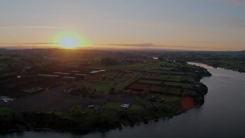 The sun is positioned low in the sky above a rural region that is bounded by a large river