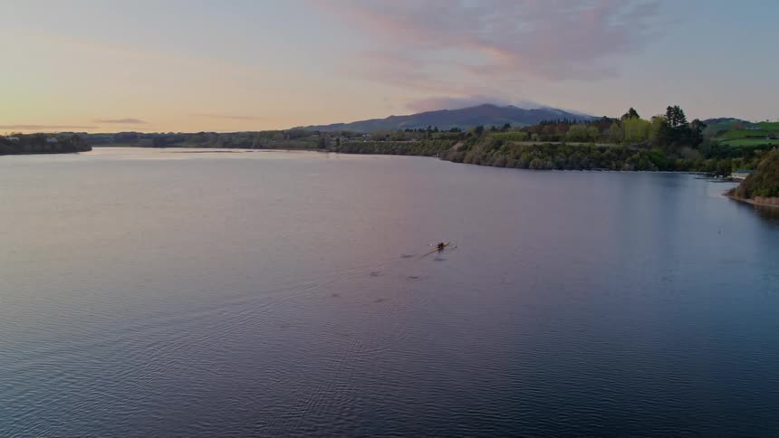 Two kayakers paddle a kayak across the lake as mountains sit in the distance
