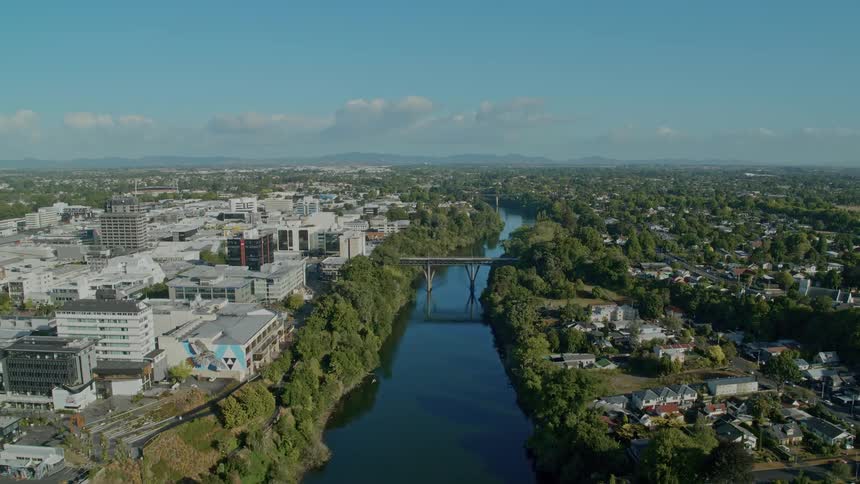 A river flanked by trees winds through a city near the mountains