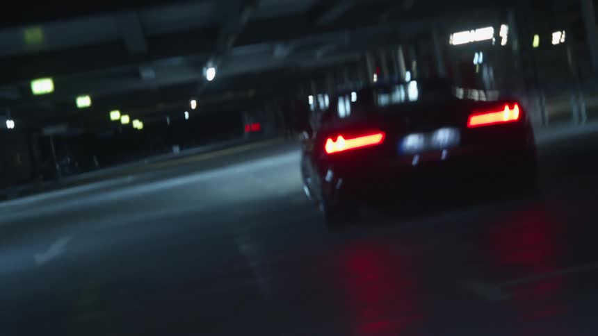 Red sports car drives in parking garage at night