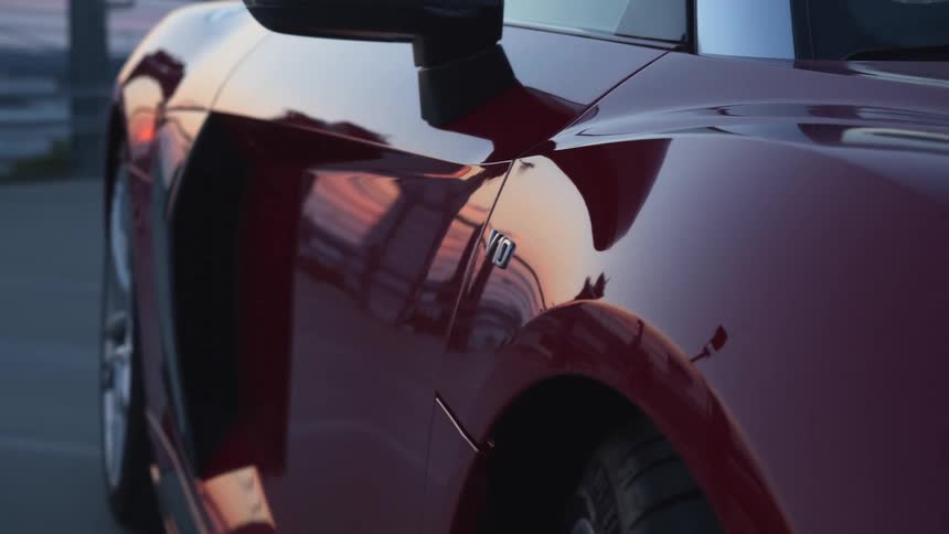 A sunset is reflected on the side of a maroon sports car