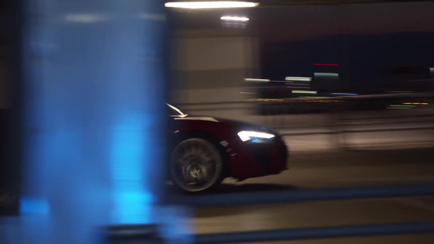 A man drives a sports car along a road through a metropolis at night