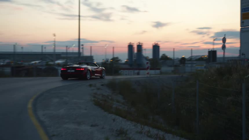 Couple drives along highway past factory with red sky on horizon