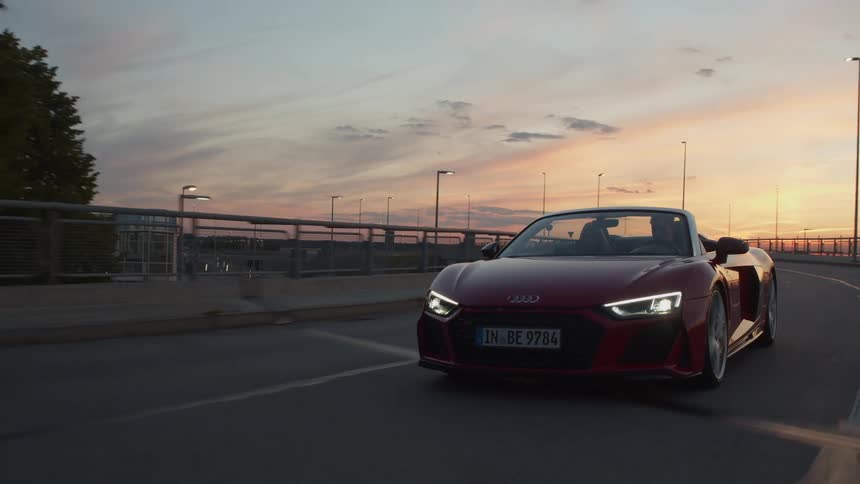 A man and woman travel down a road in a sports car at sunset