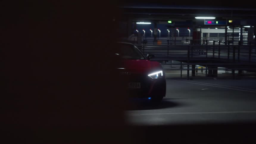 A sleek looking sports car is parked with its lights on atop a parking structure