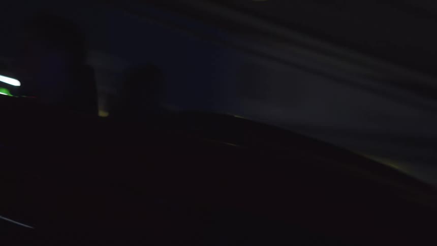 A black convertible drives through a parking garage at night