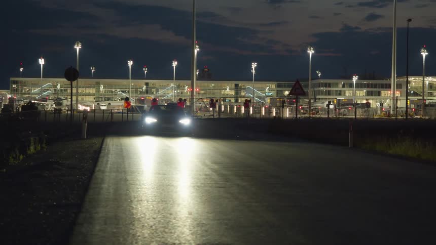 A vehicle drives on a race track at night with flashing lights behind it
