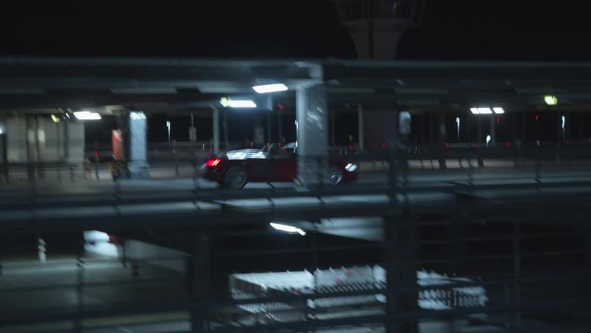 Red sports car drives on road at night