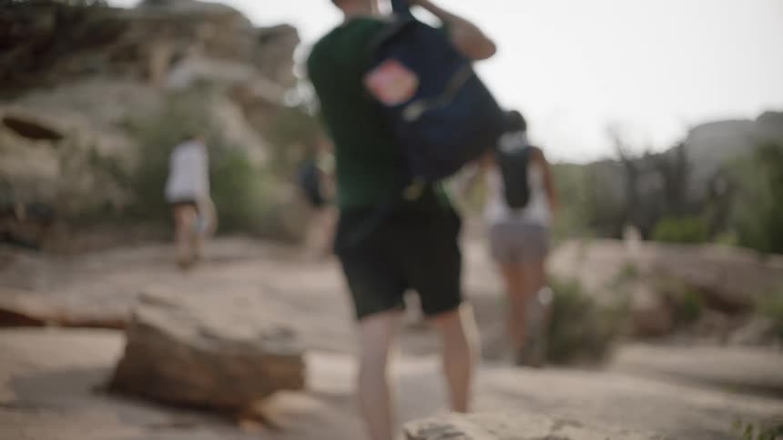 A man picks up a small backpack on a hike through a canyon