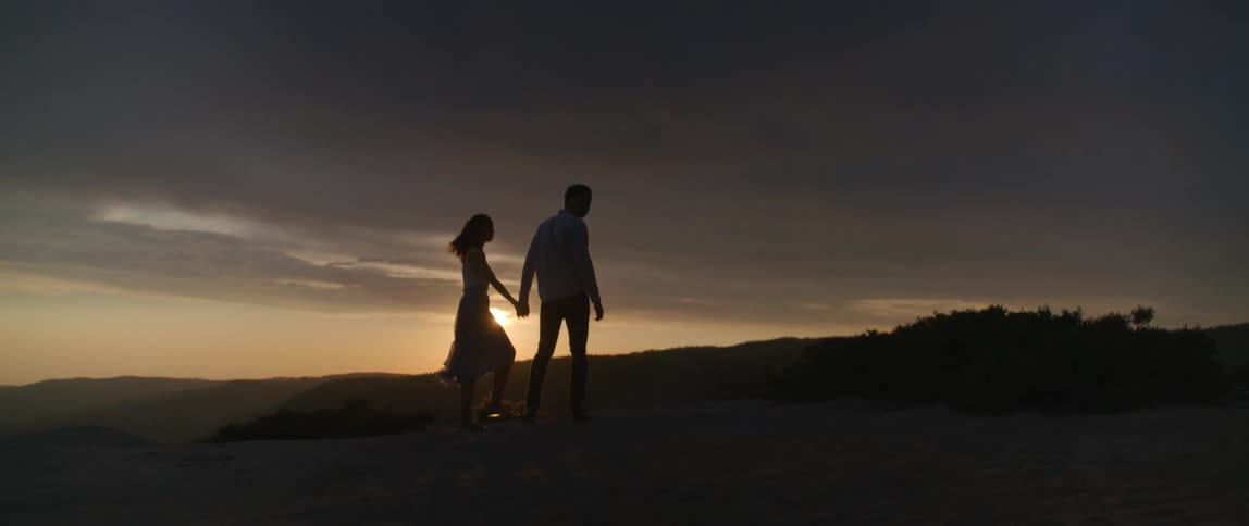 Silhouette of a couple holding hands and walking with the sun setting behind them