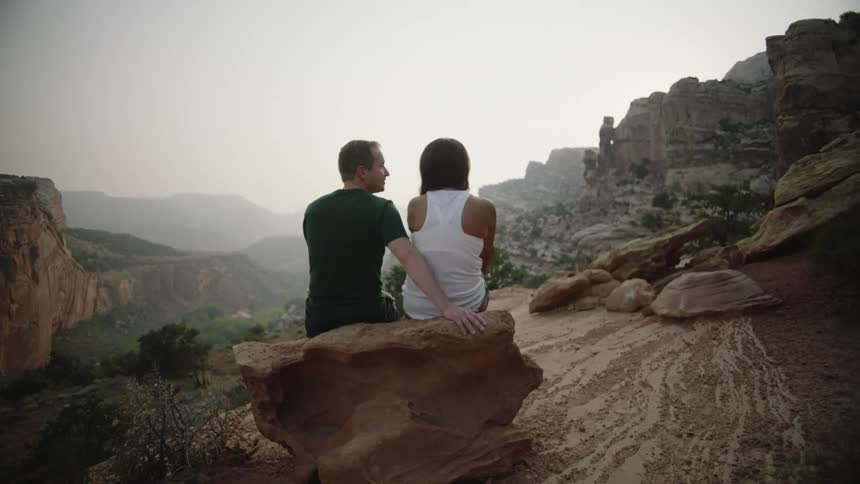 A couple sits on a rock in the mountains overlooking a foggy valley