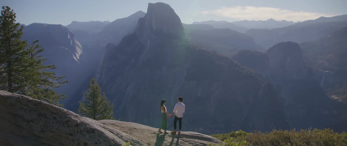 A man and woman stand on a mountain top holding hands
