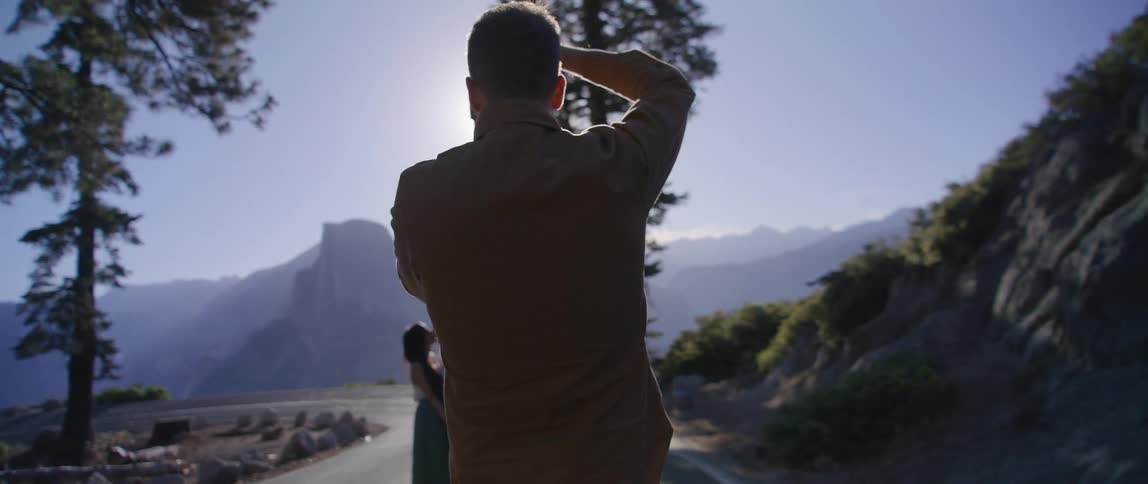 Photographer takes pictures of a young kissing couple on a road in the mountains at sunset