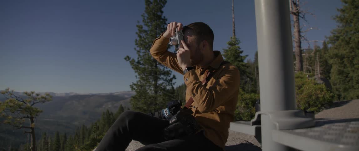 A photographer takes a picture of the forested mountain terrain in which he is sitting
