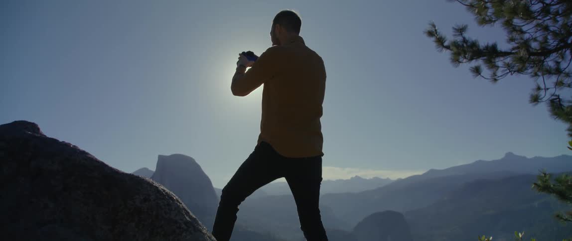 Man stands on a rock and photographs the mountains on a sunny day