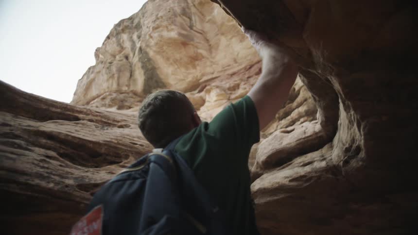 Man brushes his hand over the surface of a canyon wall at morning