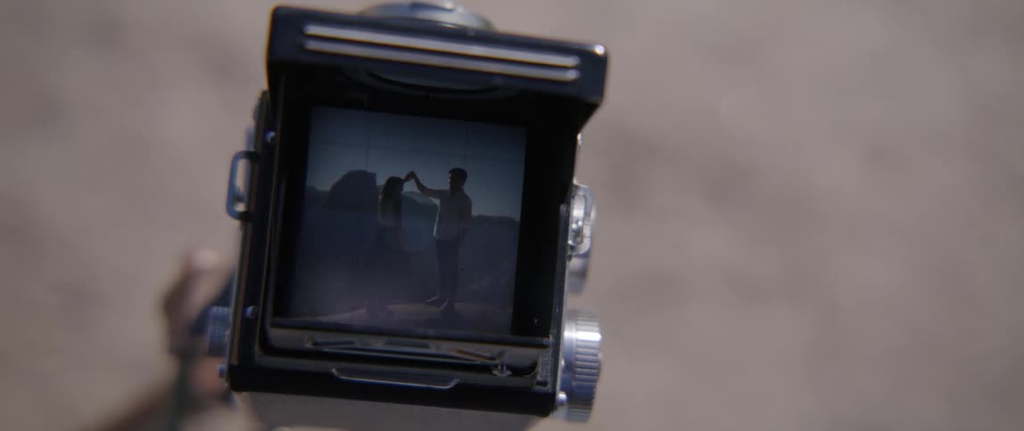 A camera with a movie of a man and a woman dancing with the ground in the background
