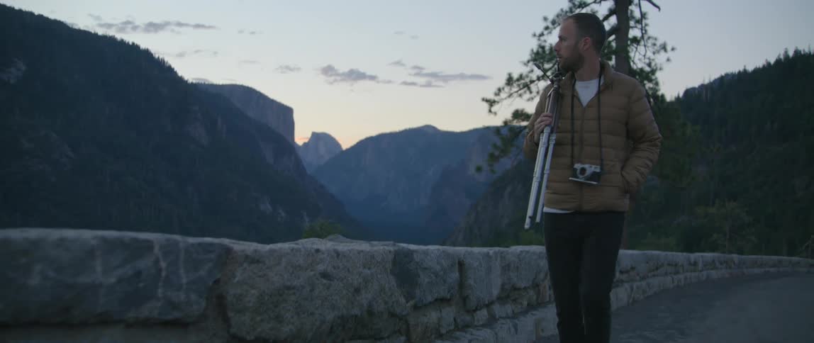 A man walks along a stone wall in front of a beautiful mountain range