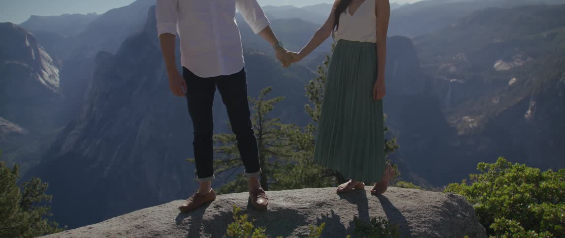 Man and woman holds hands while standing on a mountain