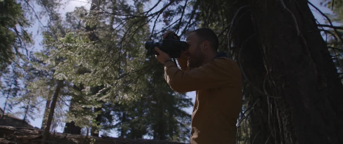 A man uses a professional camera outside in a rural woods area