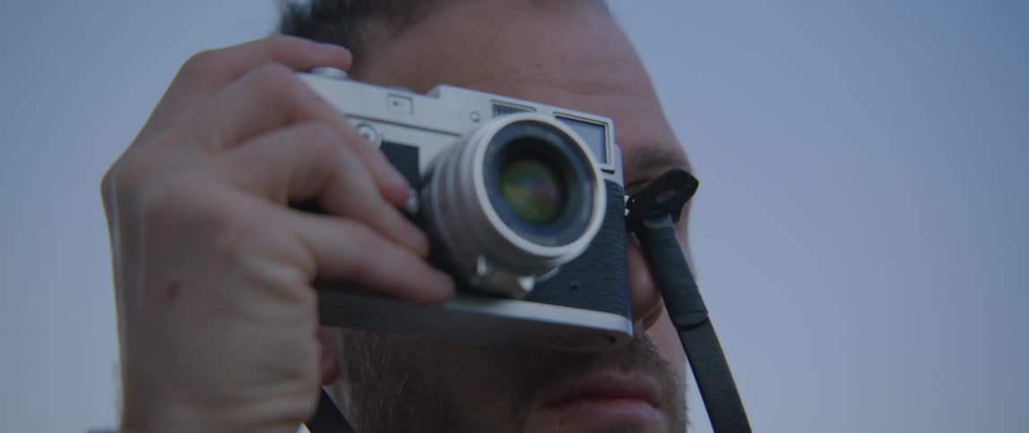 Bearded man takes pictures with a vintage camera under a blue sky at evening