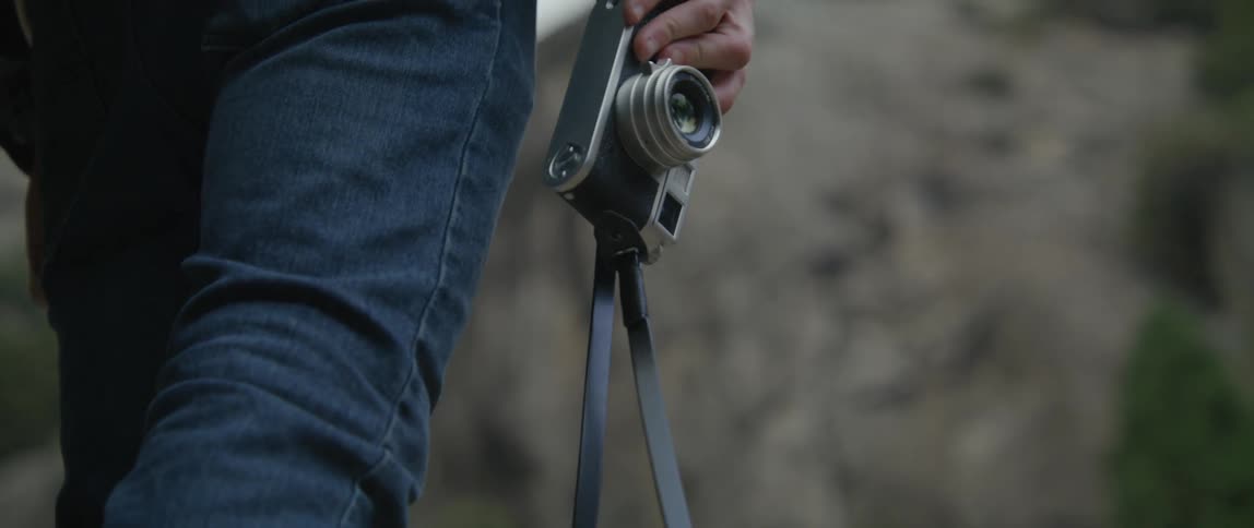 Man holds a camera at his side as he stands near the mountains