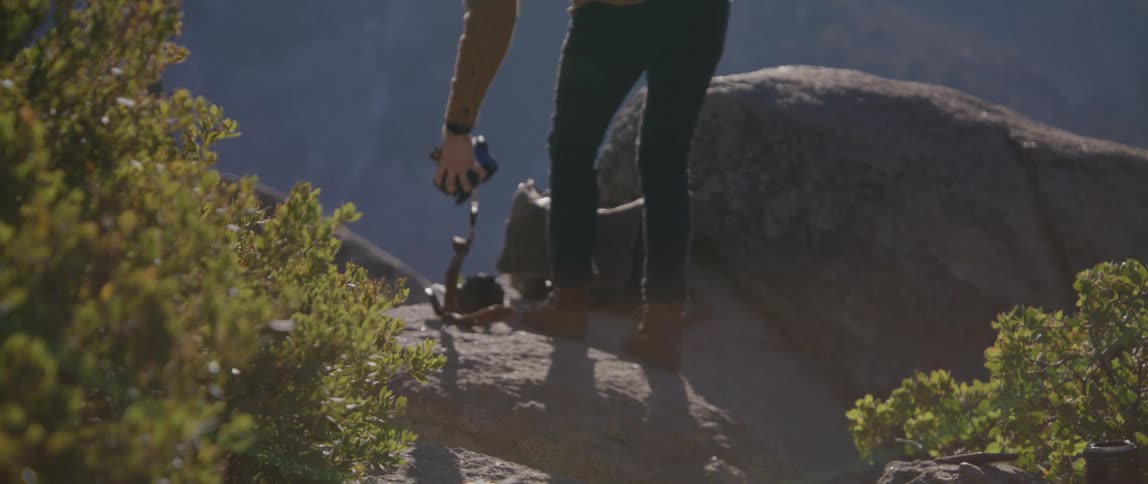 A person carries a professional camera to the edge of a mountain side